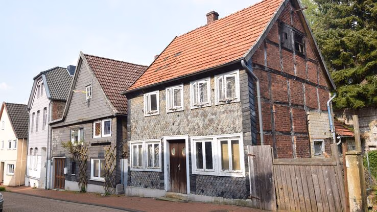 Das Bild zeigt eine Reihe traditioneller Wohnhäuser entlang einer gepflasterten Straße. Die Architektur ist geprägt von steilen Dächern, Stein- und Holzfassaden sowie weißen Fensterrahmen.