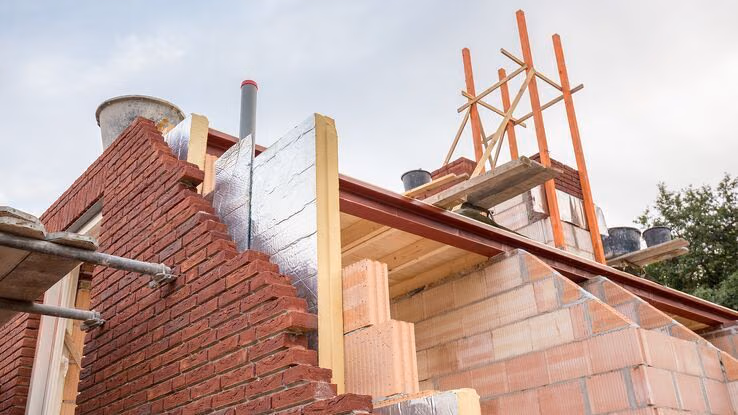 Das Foto zeigt ein Haus im Aufbau. Zwischen Außenwand und Innenwand des Hauses schaut eine Dämmplatte hervor.