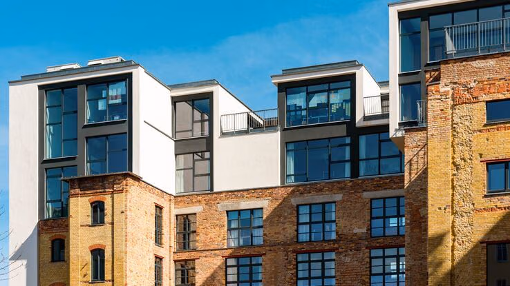 Das Foto zeigt ein älteres Gebäude aus alten Ziegelsteine. Die beiden obersten Etagen sind jedoch neu gebaut und wirken modern. Hierdurch entsteht ein Kontrast zwischen alt und modern.