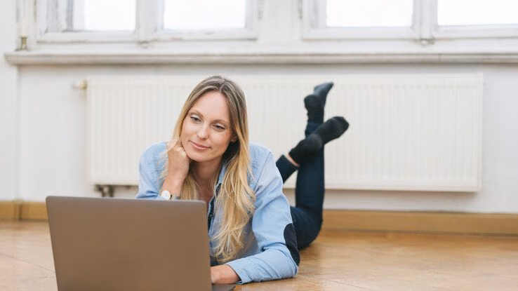 Eine Frau liegt auf dem Boden und arbeitet an ihrem Laptop.
