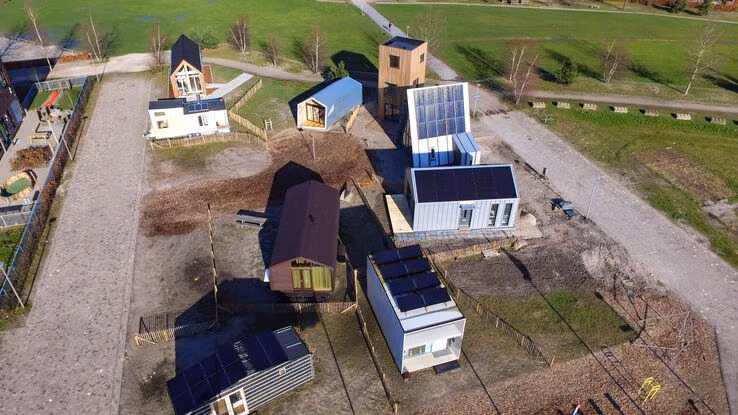Das Foto zeigt eine Tiny House Siedlung aus der Luft. Es stehen insgesamt neun Häuser, in verschiedenen Formen, nebeneinander. Einige Tiny Houses haben Photovoltaikanlagen auf den Dächern.