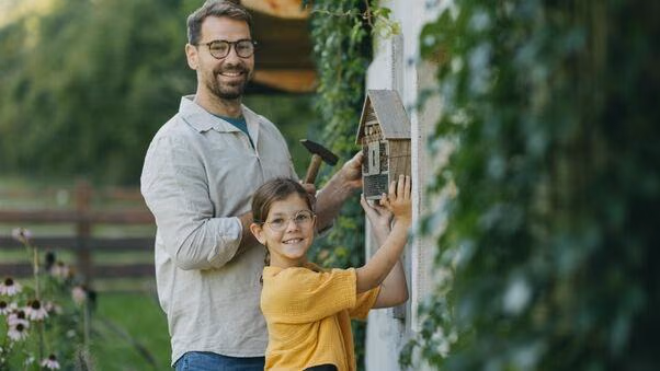 Vater und Tochter bringen im Außenbereich ein Insektenhotel an und gestalten damit ihr Eigenheim.