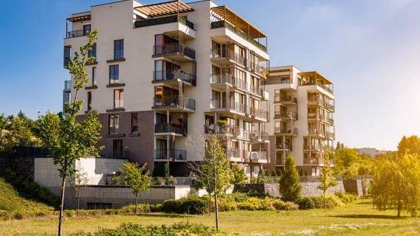 Zwei moderne Mehrparteienhäuser mit Balkonen stehen hinter einer großen Wiese.