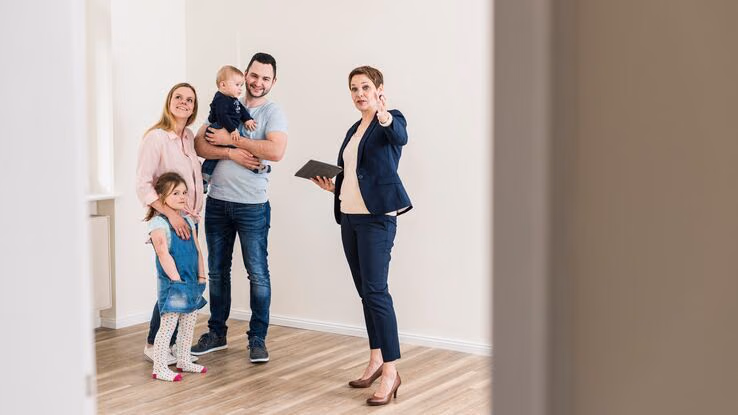 Eine Familie mit einem kleinen Mädchen und einem kleinen Jungen bekommt von der Vermieterin ihr potenzielles neues Zuhause gezeigt.